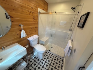 Ein Badezimmer mit einer Holzwand, einer weißen Toilette, einer Duschkabine und einem Waschbecken.