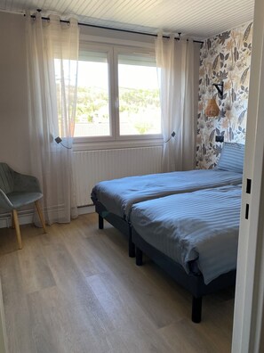 Un dormitorio con dos camas, una silla, una ventana con cortinas y una pared con un diseño de hojas.