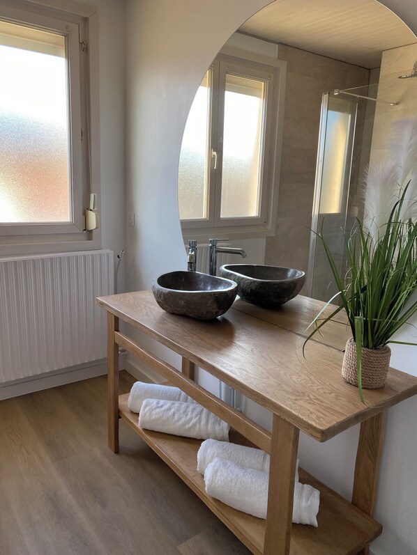 Ein Badezimmer mit Holzwaschtisch, zwei Waschschalen, einem Spiegel, einer Topfpflanze und einem Handtuchhalter.