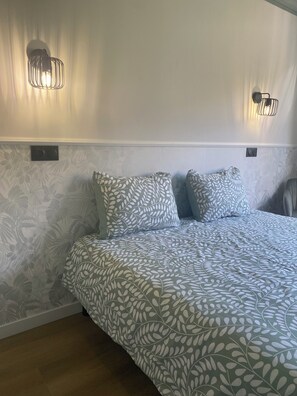 Un dormitorio con cama, pared con diseño y dos lámparas fijadas a la pared.