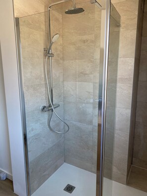 Eine begehbare Duschkabine mit Handbrause und am Wand montiertem Wasserhahn.