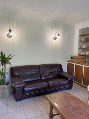 A brown leather sofa, a wooden coffee table, a potted plant, and a cabinet with a sign.