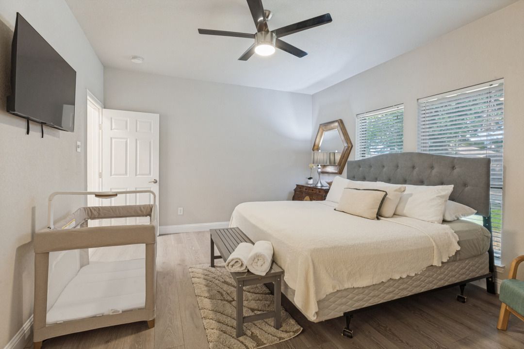 A bedroom with a bed, a ceiling fan, a TV, a bunk bed, and a window with blinds.