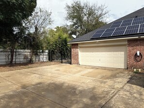 A residential garage with a white garage door, solar panels on the roof, and a brick exterior wall. - AT&T Stadium - 3BR 2BA Home Parking EV (Arlington)