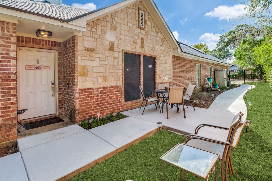 A brick building with a door labeled 'AMERICA'S BEST,' a patio with outdoor furniture, and a well-maintained lawn.