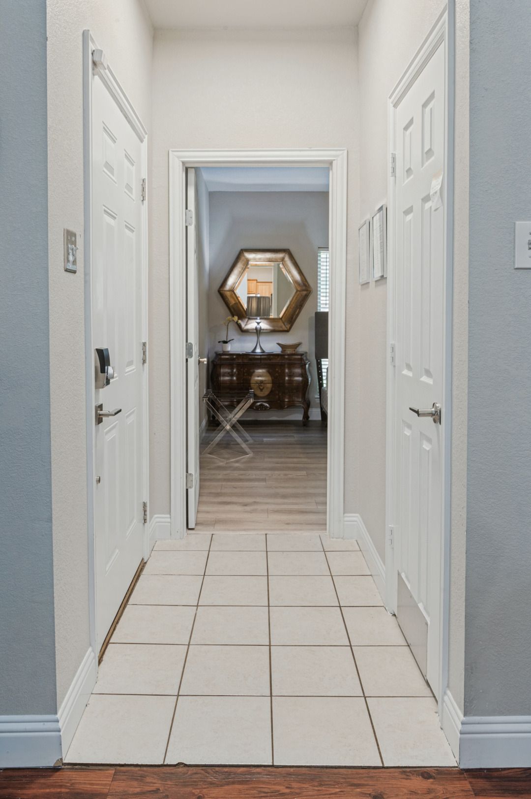 A hallway with white doors, a wooden floor, and a mirror on a dresser.