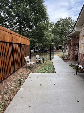 A patio area with a concrete floor, metal chairs, and a wooden fence. - AT&T Stadium - 3BR 2BA Home Parking EV (Arlington)