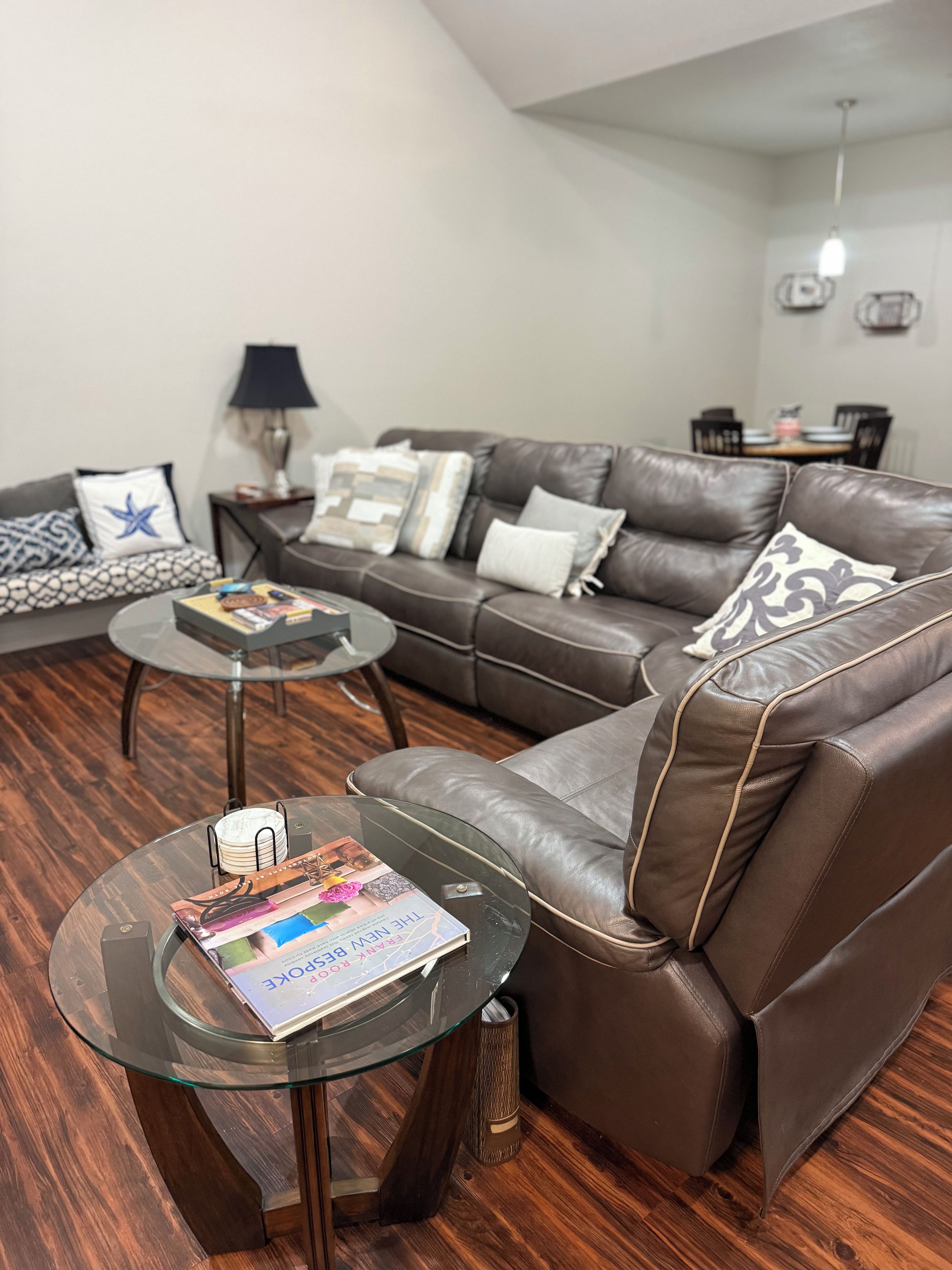 Ein modernes Wohnzimmer mit Ledersofa, Glastisch und einem Essbereich im Hintergrund.