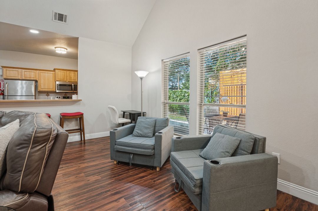 A modern living room with a sofa, two armchairs, a small table, and a kitchen area with wooden cabinets and appliances.