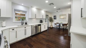 Uma cozinha moderna com armários brancos, eletrodomésticos de aço inoxidável e um espaço de refeições com mesa e cadeiras.