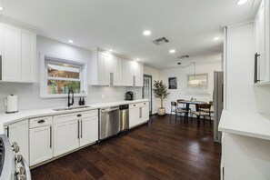 A modern kitchen with white cabinets, stainless steel appliances, and a dining area with a table and chairs. - Designer Pool Retreat (Houston)