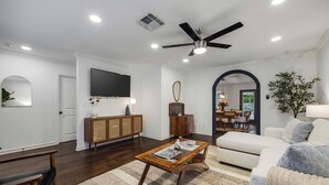 Uma sala de estar com sofá, mesa de centro, televisão e ventilador de teto.