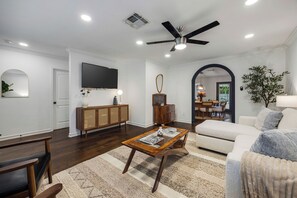 A living room with a sofa, coffee table, TV, and a ceiling fan. - Designer Pool Retreat (Houston)