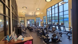 Una palestra con diverse attrezzature per l'allenamento, ampie finestre e uno schermo televisivo.