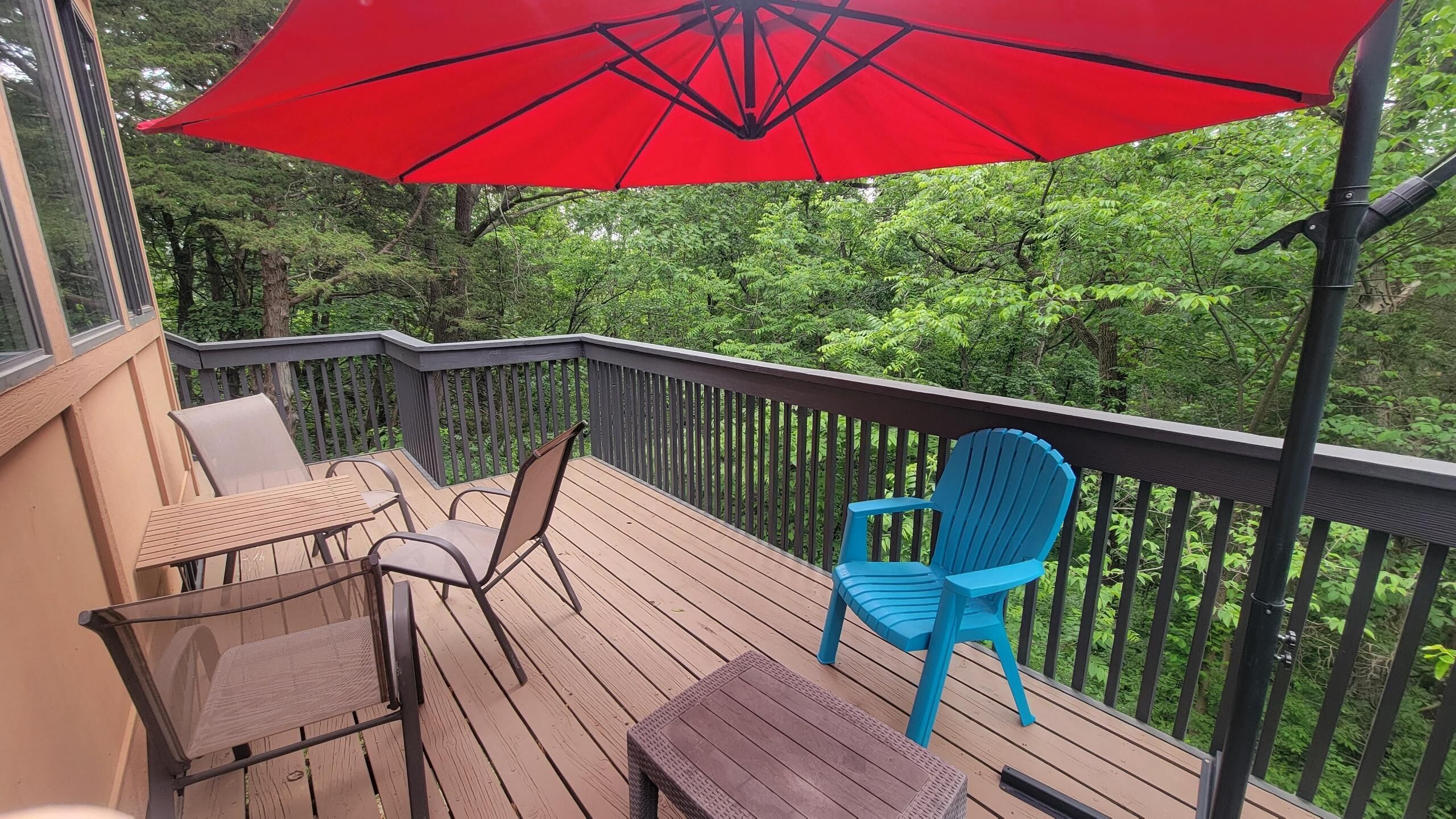 A wooden deck with a red umbrella, two chairs, and a table.