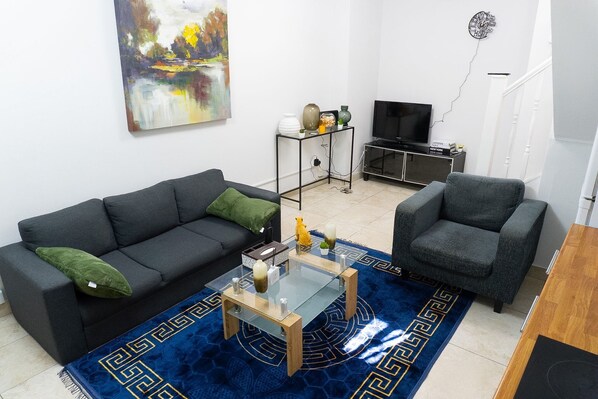 A living room with a sofa, armchair, coffee table, TV stand, and artwork.