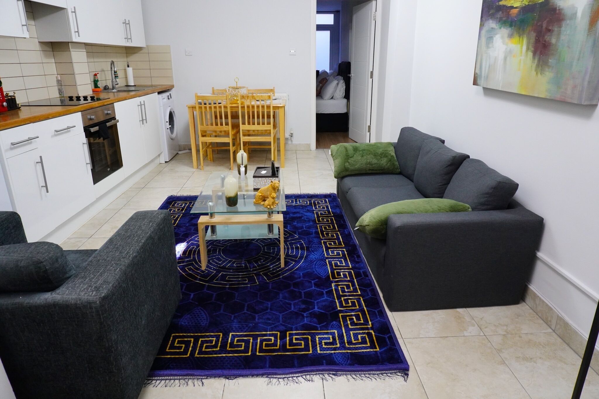 Un espace de vie compact comprenant un canapé, une table basse, une table à manger avec des chaises, un lave-linge et un coin cuisine.
