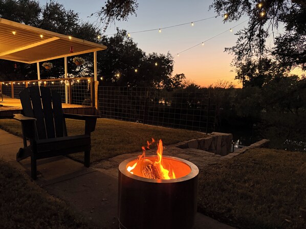 A patio area with a fire pit, outdoor seating, and string lights.