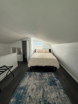 Un dormitorio con cama, ventana, puerta y una mesita.