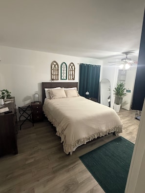 Un dormitorio con cama, escritorio, silla, reloj y alfombra verde.
