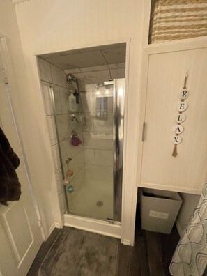 A bathroom with a glass-enclosed shower, a white cabinet with a towel rack, and a wall-mounted sign spelling 'RELAX'. - 3-bedroom Lakefront Barndominium - 12 minutes to downtown Granbury with AC (Granbury)