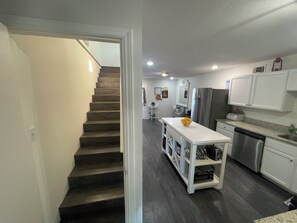 Una cocina moderna con una isla central, electrodomésticos de acero inoxidable y una escalera de madera oscura.