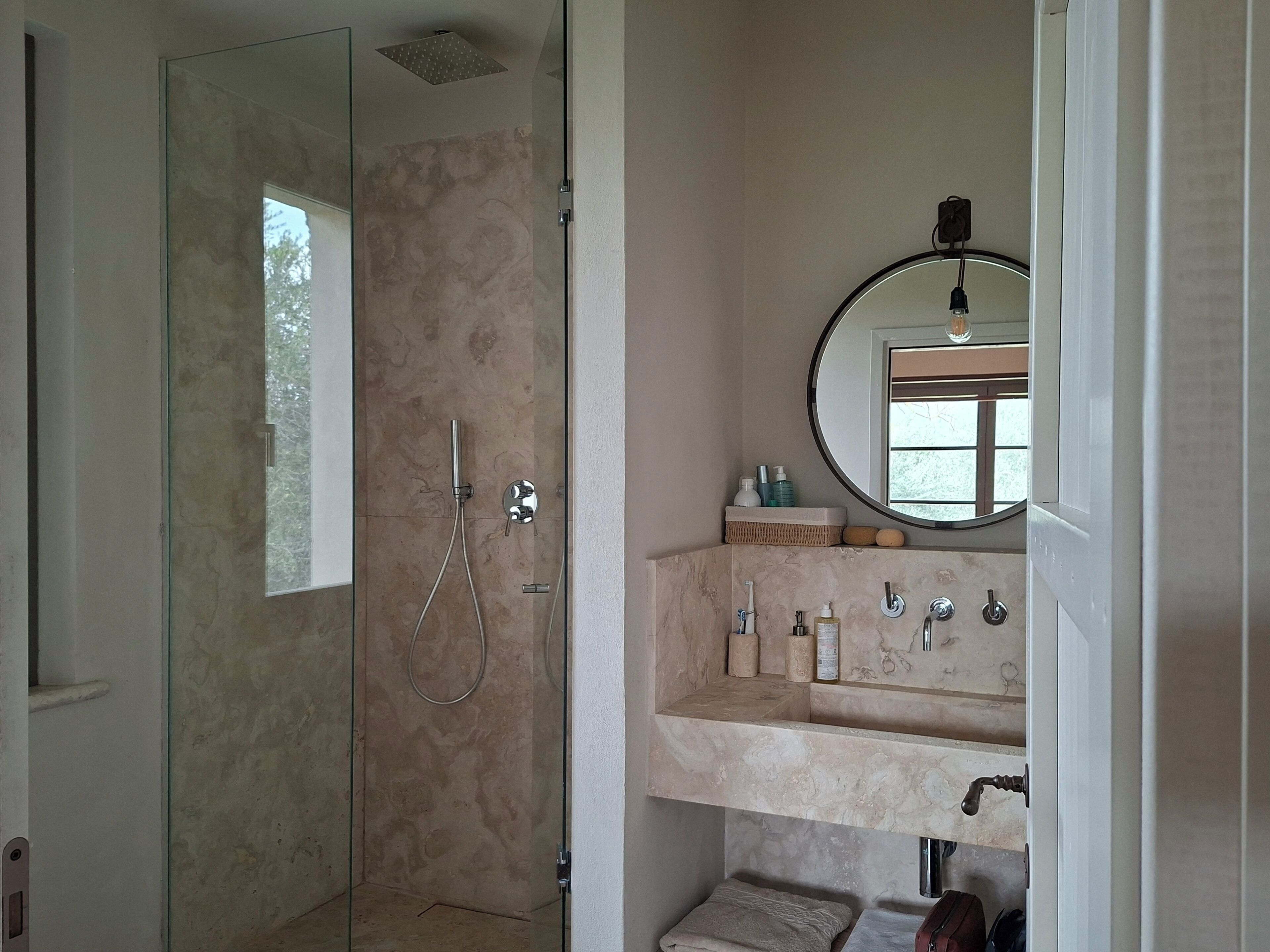A bathroom with a glass-enclosed shower, a sink with a mirror, and toiletries.