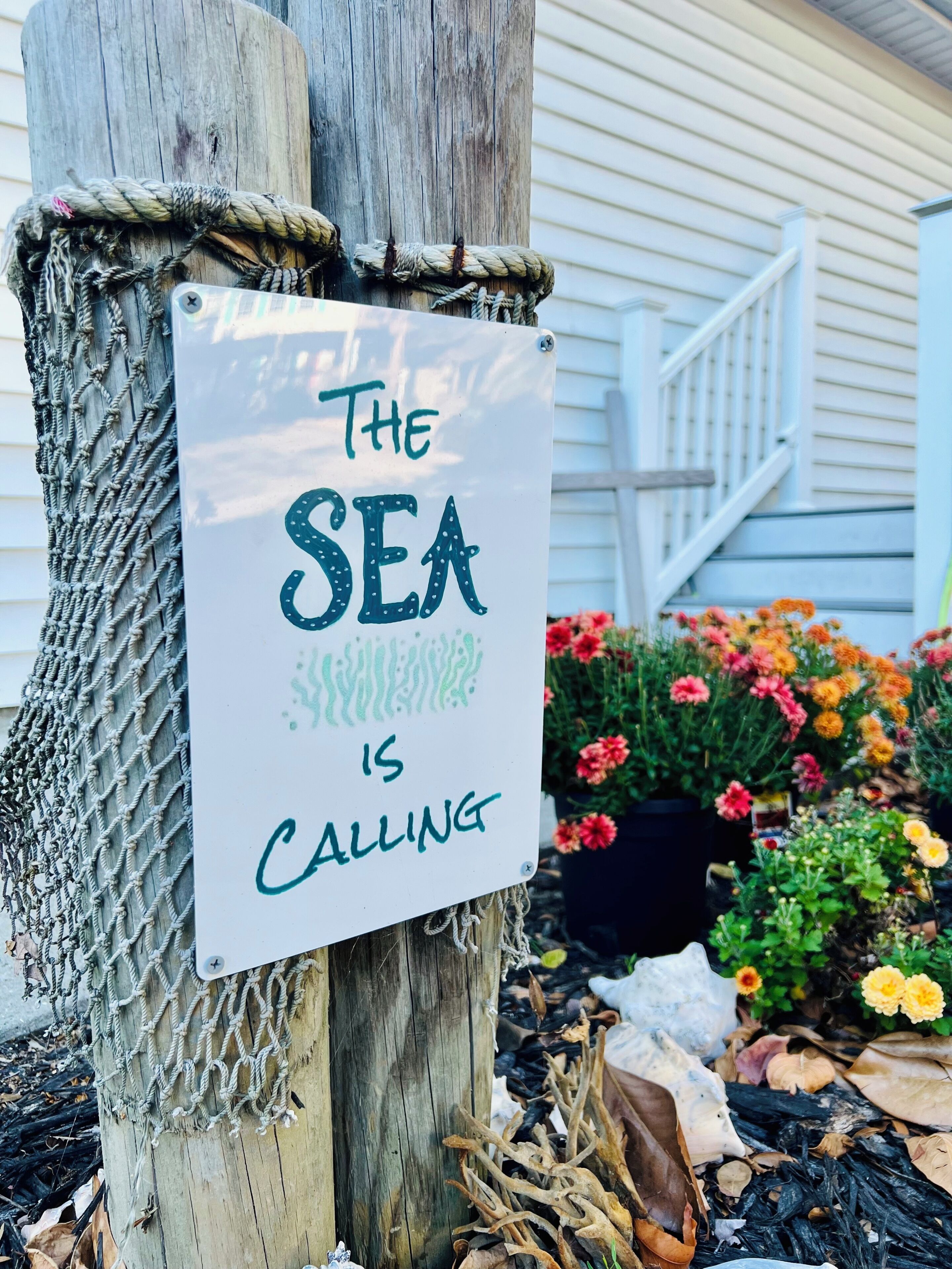 A wooden post with a sign that reads 'The SEA IS CALLING.'