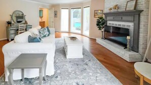Una sala de estar con chimenea, un sofá blanco, una mesa de centro y una mesita auxiliar.