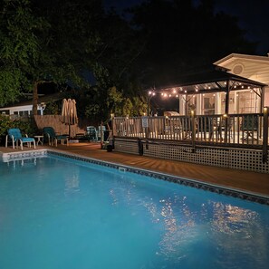 Ein Swimmingpool mit Liegestühlen, einer Holzterrasse und einem überdachten Bereich mit Lichterketten.