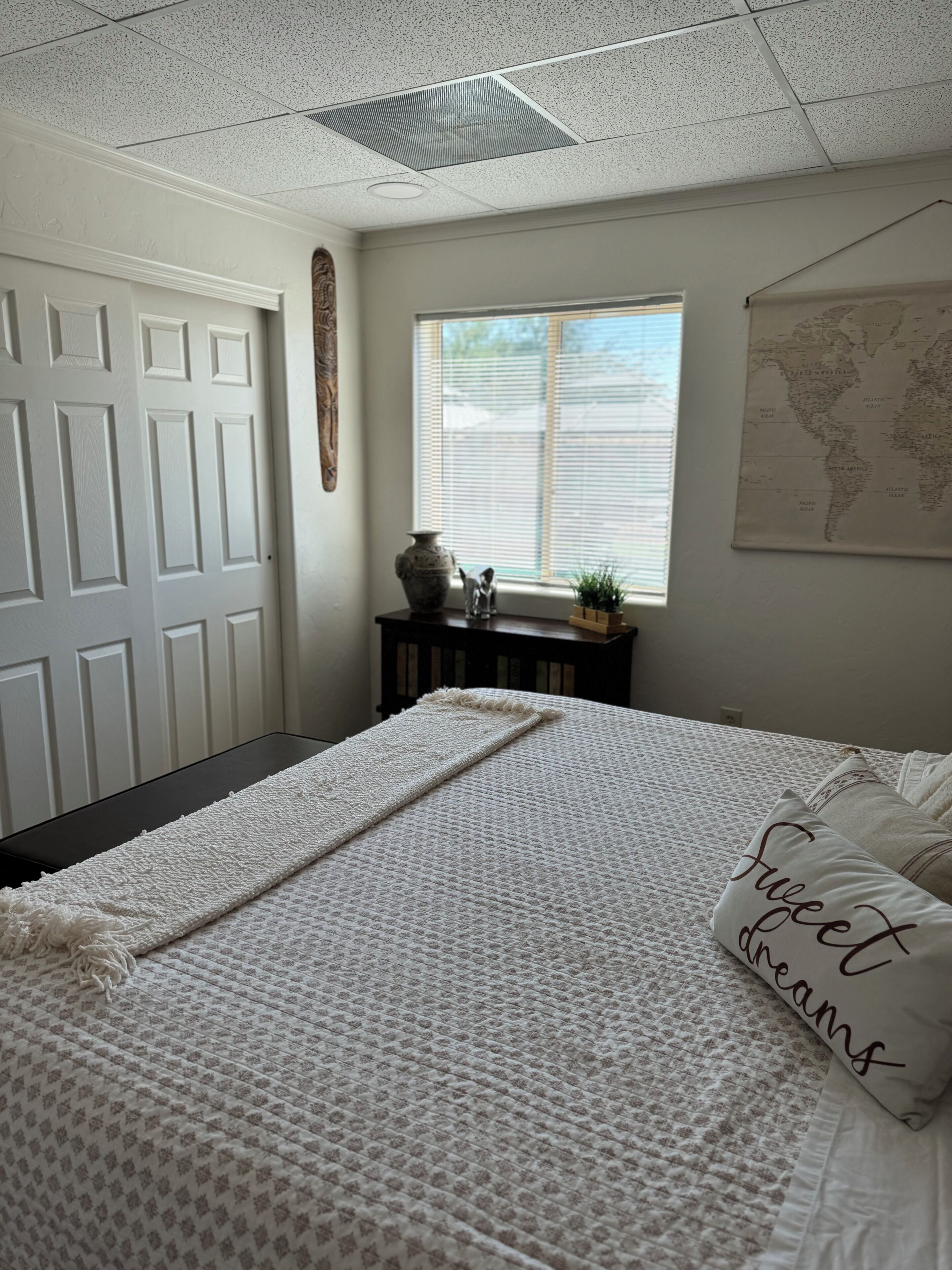 Un dormitorio con cama, ventana con persianas, mapa en la pared y una puerta.