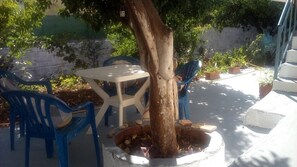 Ein Sitzbereich im Freien mit Tisch und Stühlen, einem Baum und Kübelpflanzen.