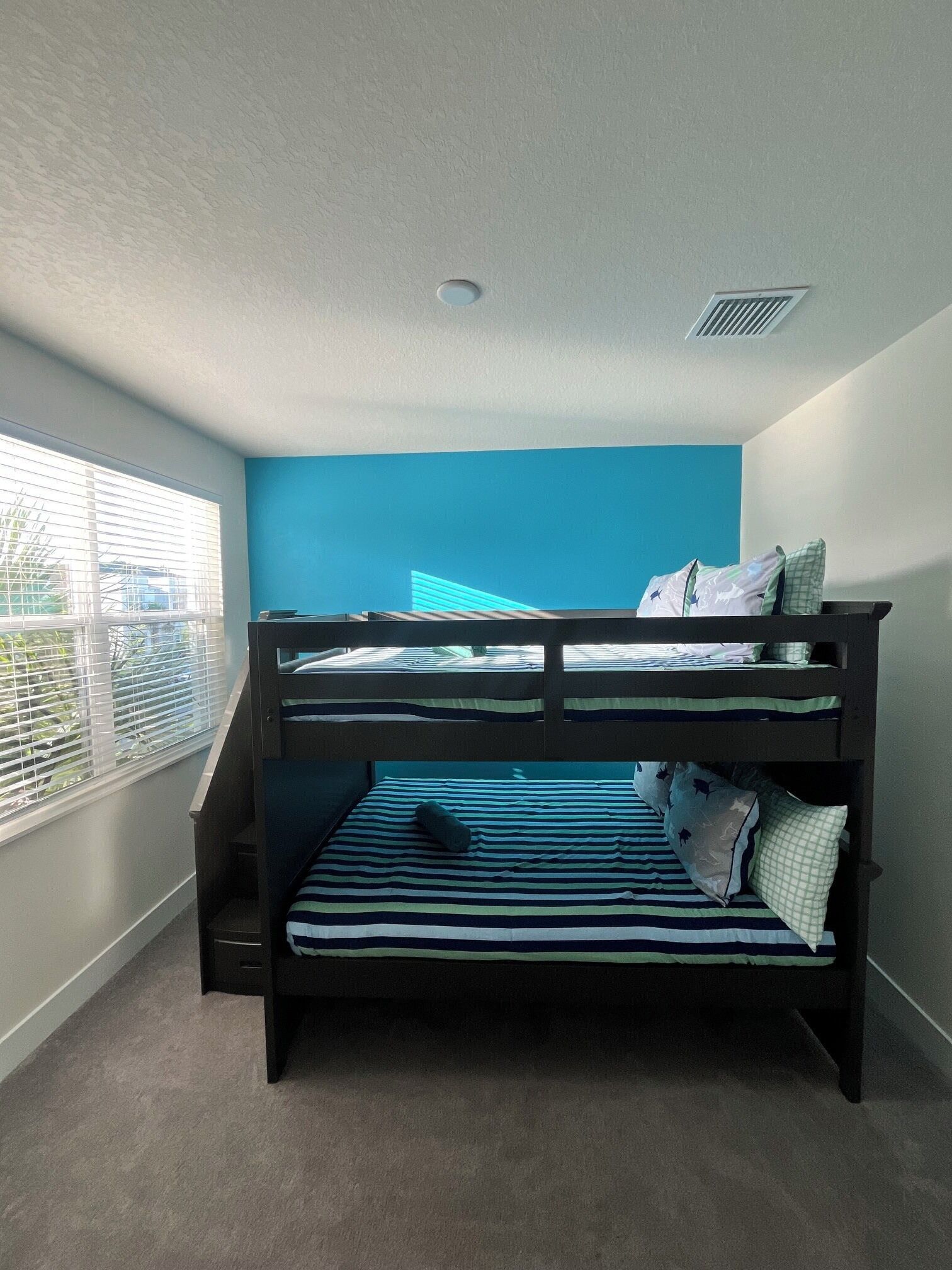 Een slaapkamer met stapelbed, raam, dakraam en een blauwe muur.