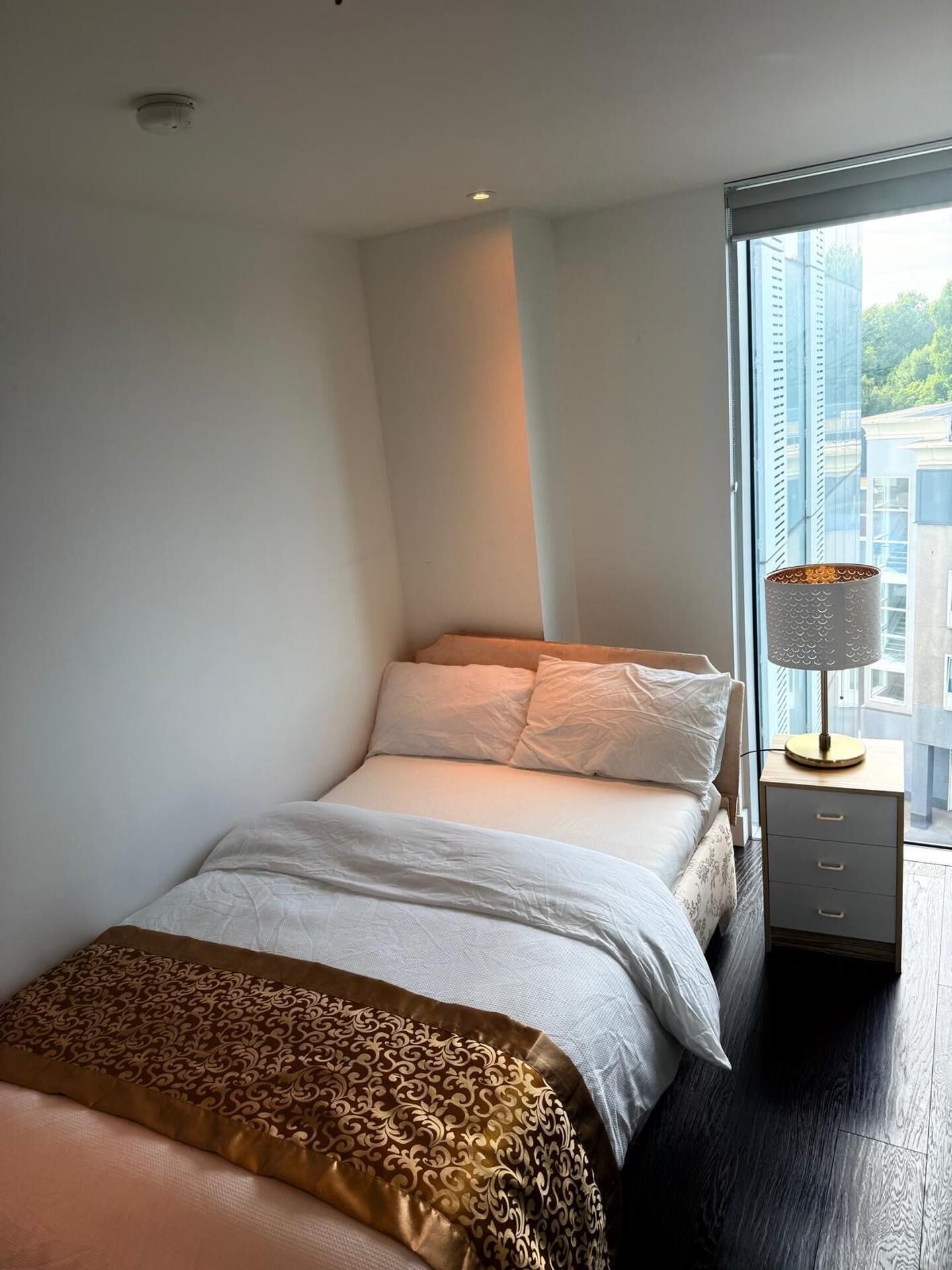 Una camera da letto moderna con un letto, un comodino e vista sugli edifici attraverso una finestra.