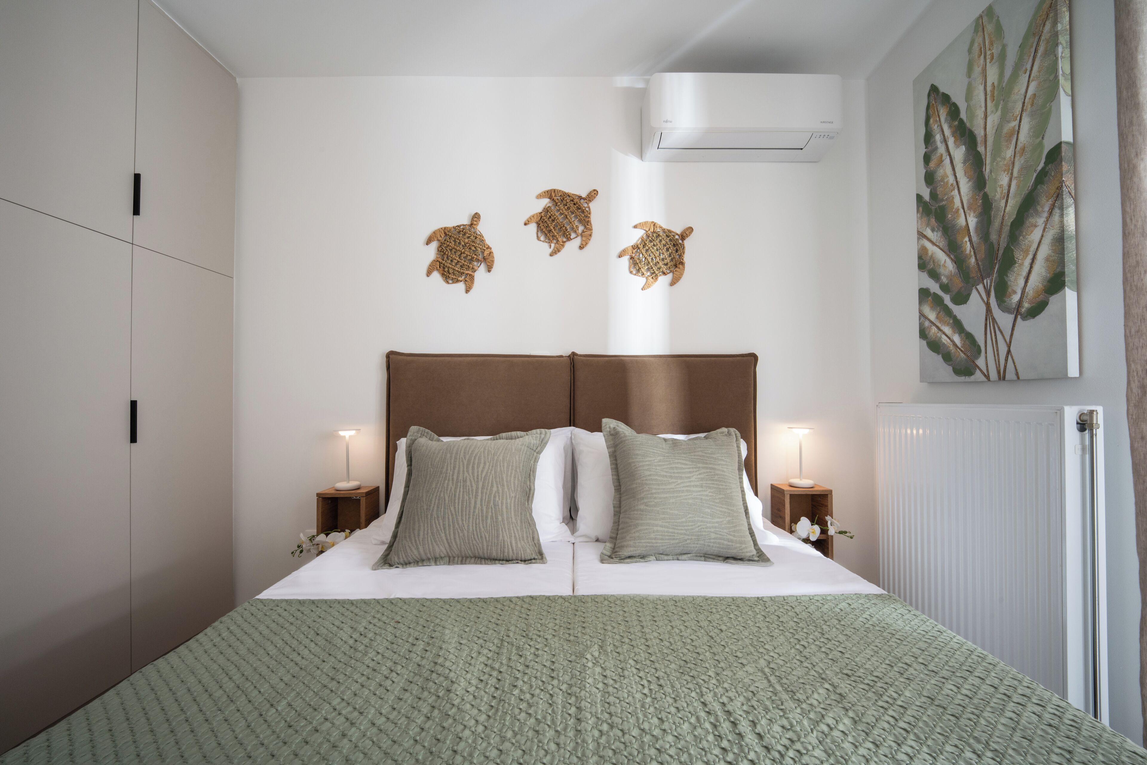 A hotel room with a bed, two bedside tables, a wall-mounted air conditioner, and a large window.