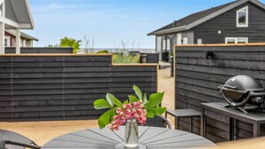 Eine Terrasse mit rundem Tisch, einem Grill und einem Blumenvasen.