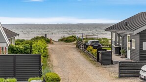 Ein Anwesen an der Küste mit einem Schotterweg, der zum Strand führt, einem geparkten Auto und einem Haus mit dunkler Fassade.