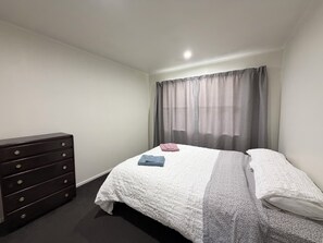 A bedroom with a bed, a dresser, and a window with curtains.