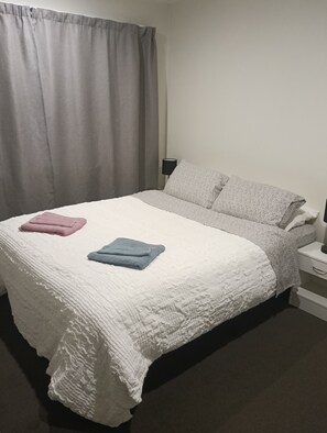 Un lit avec une couette blanche, deux oreillers et deux serviettes pliées.