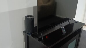 Un meuble noir pour équipements de divertissement, comprenant un téléviseur à écran plat, une télécommande et un haut-parleur.