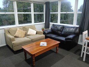 Un salon avec un canapé beige, un canapé en cuir noir, une table basse en bois et une chaise blanche.