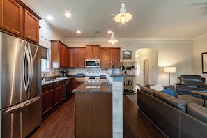 A modern kitchen with stainless steel appliances, wooden cabinets, a central island, and a seating area with a leather couch.