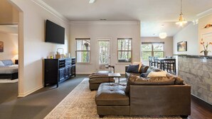 A living room with a sectional sofa, a flat-screen TV, a ceiling fan, and a dining area with a table and chairs.