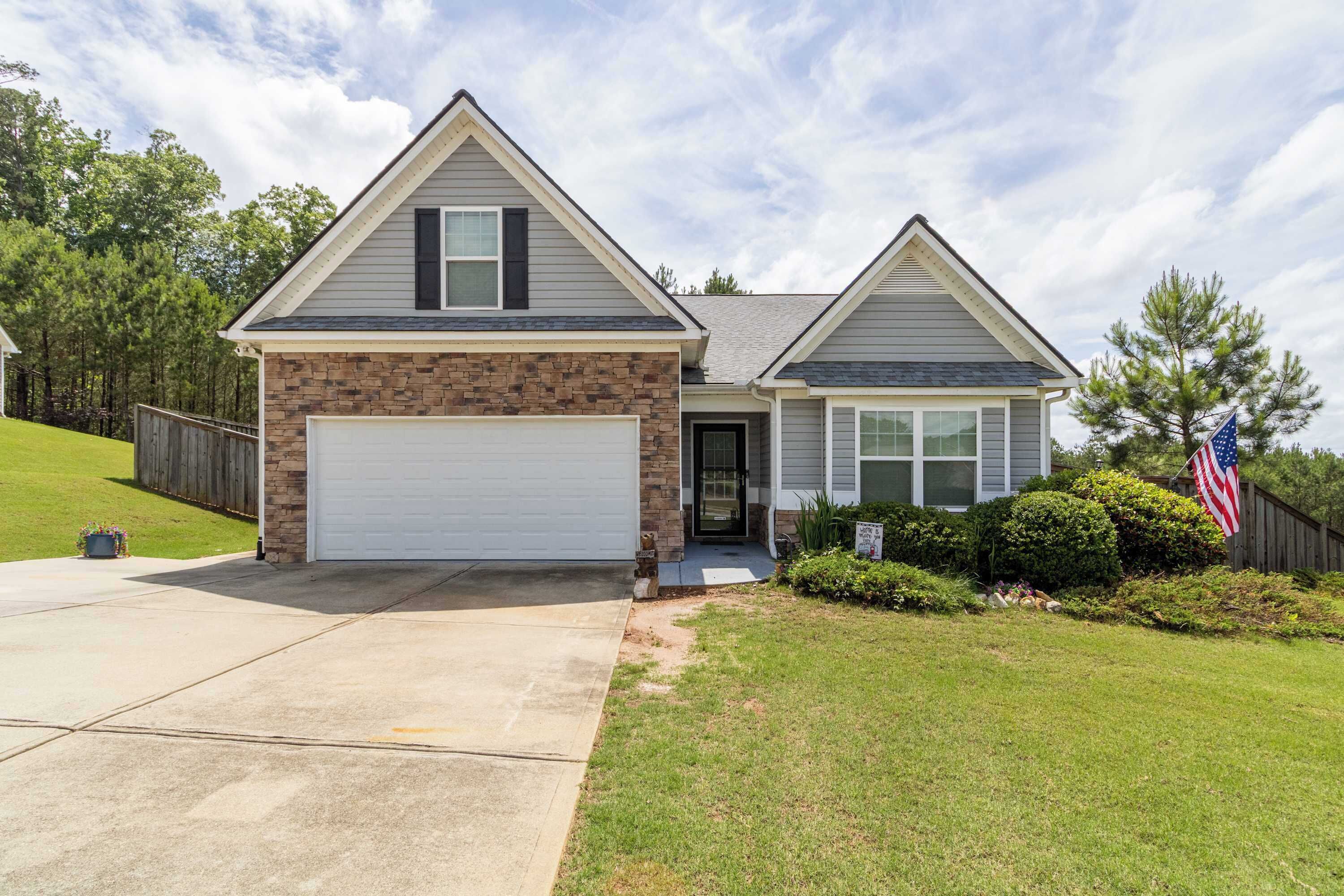 A two-story house with a garage, a front door, and a small front yard with a lawn and a flag.