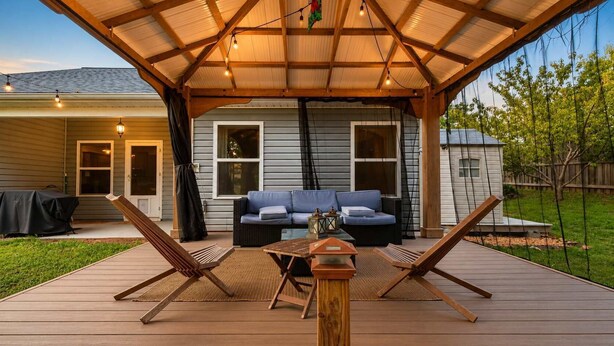 A covered patio with a wooden deck, a blue sofa, two lounge chairs, and a small table.