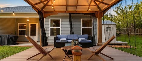 Une terrasse couverte avec une plateforme en bois, un canapé bleu, deux fauteuils et une petite table.