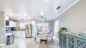 A modern kitchen with white cabinets, a stainless steel refrigerator, a dining area with a round table and chairs, and a blue cabinet with glass doors.