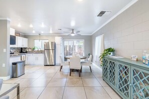 Una cocina moderna con armarios blancos, un refrigerador de acero inoxidable, una zona de comedor con mesa y sillas redondas, y un mueble azul con puertas de vidrio.