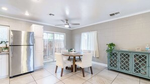 A kitchen with a stainless steel refrigerator, a dining table with chairs, a ceiling fan, and a cabinet with a lattice design.