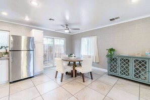 Una cocina con un refrigerador de acero inoxidable, una mesa de comedor con sillas, un ventilador de techo y un mueble con diseño de celosía.
